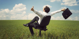 businessman in field with blue sky sitting an office chair
